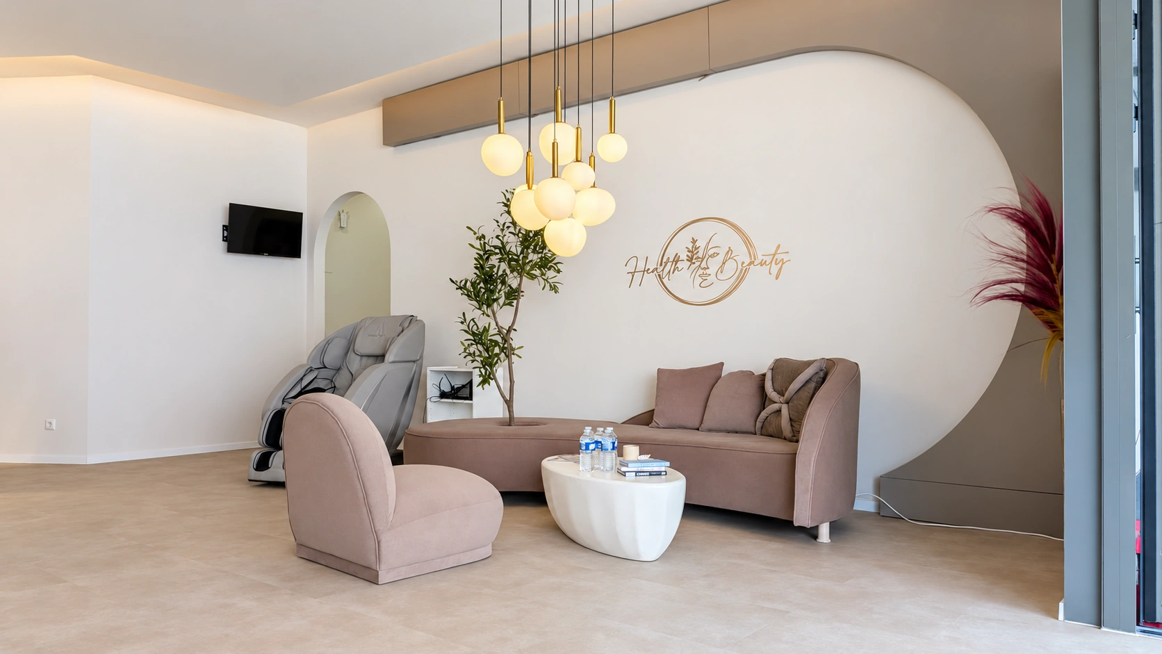 H&B-Studiolounge mit taupefarbenen Sitzmöbeln, Kugelleuchten und originalem Wandlogo, fotografisch aufgehellt.
