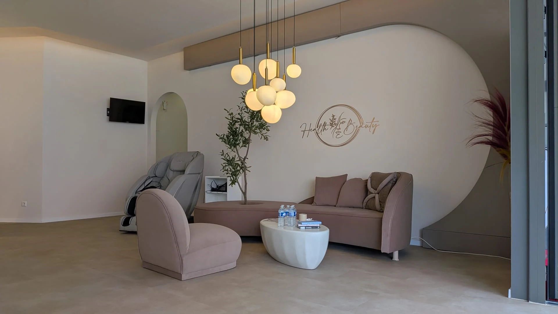 Wartebereich im H&B-Studio mit geschwungenem Sofa, Kugelleuchten und goldenem Wandlogo.